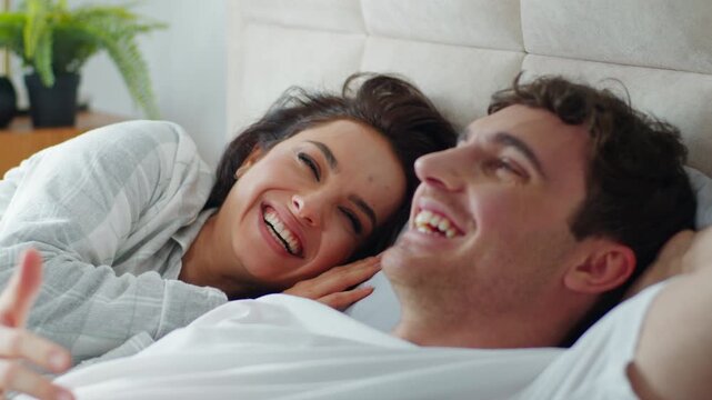 Happy Caucasian couple man woman lying on bed at home bedroom discussing plans chatting talking laughing girlfriend boyfriend honeymoon romance togetherness intimate love affection relax family smile