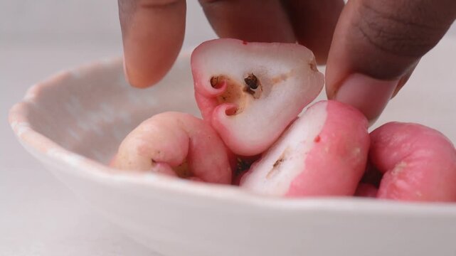 sliced and whole bruised rose apples on a white stone background, whole pink rose apples on a white background