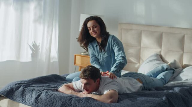 Happy Caucasian couple woman massaging man back on bed at home bedroom healthy laugh smiling rest relaxation weekend female male boyfriend girlfriend love support care sweetheart tender husband wife