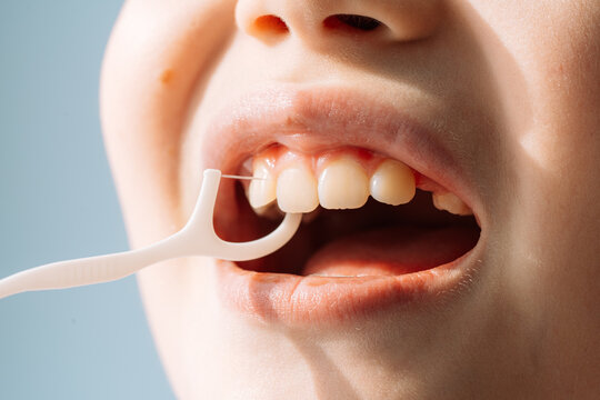 Close up child using a floss pick between teeth, kids dental hygiene routine.