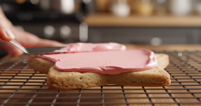 A person frosting a freshly baked star-shaped cookie with pink icing in a cozy kitchen setting