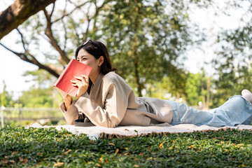 Young asian woman relaxing reading book sitting at public park life style outdoor. Happy female Take a break enjoy time living in the nature. Human and nature together