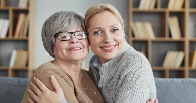 Smiling daughter and senior mother hug warmly. A warm family portrait at home conveys care, support, and intergenerational bonding with a cozy background and natural light. Good for home care ads.