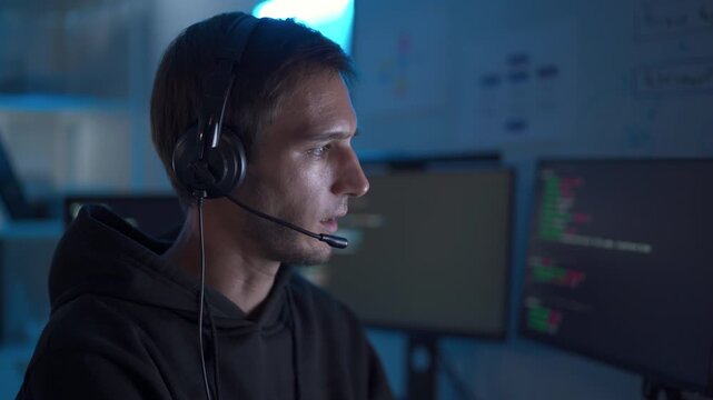 Software developer working at computer with headset in dark office coding environment