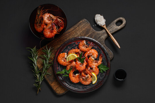 Plate of tasty boiled shrimps with parsley and lemon on dark background
