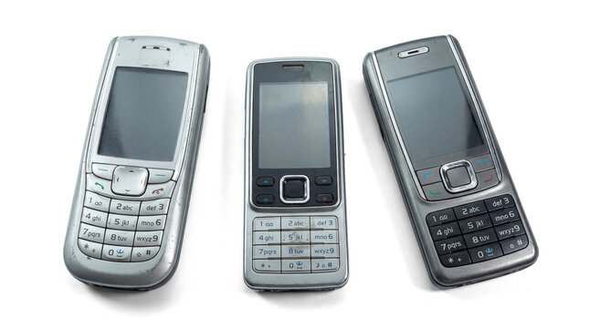 three classic silver mobile phones with physical keypads, viewed from an angle against a transparent background, representing early mobile device technology.