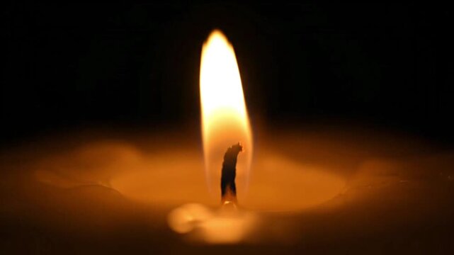 Close up of a candle flame burning in darkness creating warm light and peaceful atmosphere.