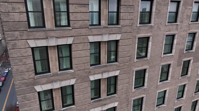 Aerial drone shot rising along facade of downtown apartment building in an American city, revealing rows of windows and classic urban architecture in dense metropolitan district.