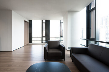 Fototapeta premium Modern minimalist living room with black leather sofa and armchair on wooden flooring near floor-to-ceiling windows