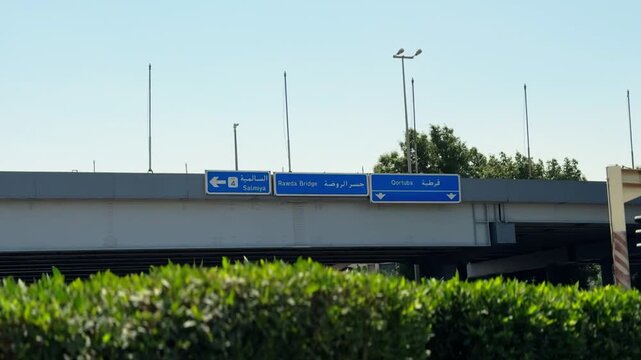 Road direction signs on an urban highway overpass in Kuwait indicating Salmiya, Rawda Bridge, and Qortuba with bilingual Arabic and English text under clear daylight sky.