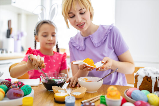 A mother and daughter are happily dyeing and decorating Easter eggs together in a bright kitchen setting