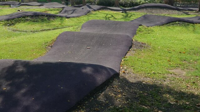 Curved smooth dark paved skateboard pump track pathway winding through bright green lawn grass in urban park landscape design
