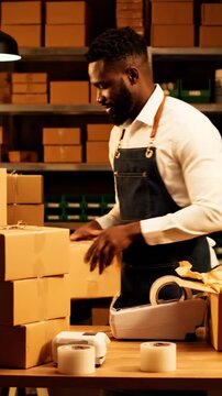 Focused Man Packing Orders in Warehouse with Shelves of Boxes and Warm Lighting