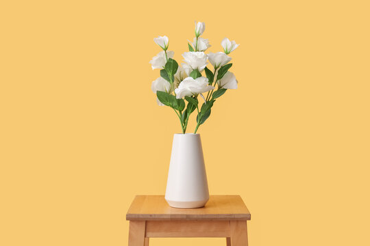 Vase with artificial eustoma flowers on table against yellow background