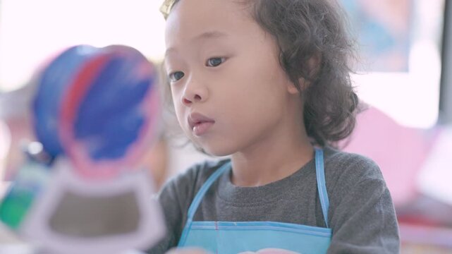 Young child learning painting while decorating a plaster figurine with a brush, developing artistic skills, creativity, concentration, imagination.