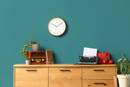 Vintage typewriter, telephone and radio receiver on wooden chest of drawers in interior of living room, closeup