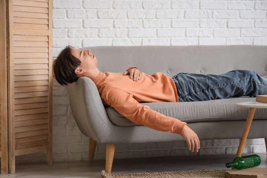 Drunk young man sleeping on sofa at home after party
