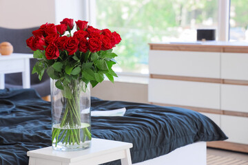 Naklejka premium Vase with beautiful red roses on bedside table in stylish bedroom