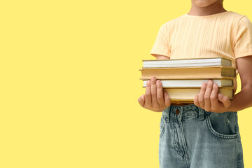 Fototapeta premium Cute little girl holding books on yellow background