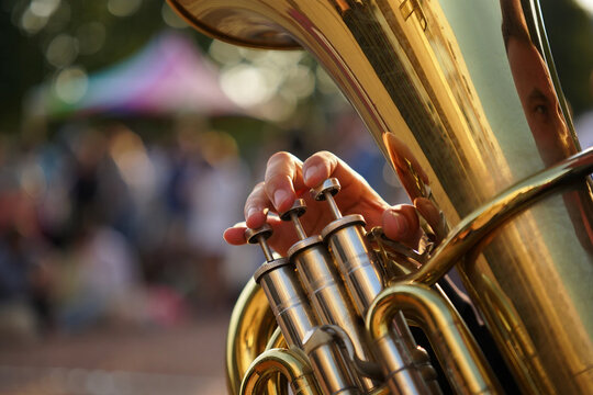 Jazz Day Hand playing brass euphonium instrument with blurred outdoor crowd background