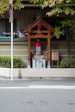 Japanese roadside shrine with jizo statue wearing red bib under wooden roof in urban street