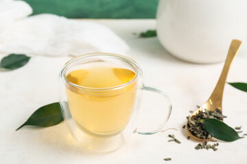 Glass cup of hot green tea and dried leaves on white table