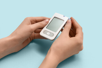 Young diabetic woman using digital glucometer on blue background
