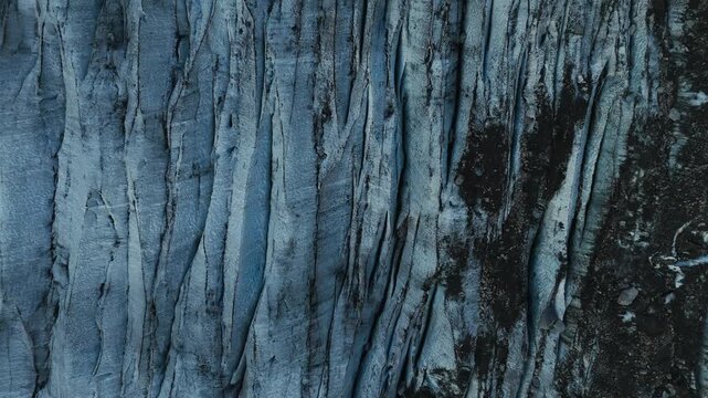 Blue glacier ice surface with dark crevasses and textured patterns in Norway, top-down drone close-up