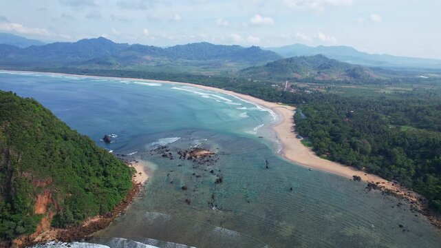 Aerial drone footage of the rocky hill in Red Island beach, Banyuwangi regency, Java island, Indonesia, with a beautiful crystal sea, and a white sandy bay beach, clear reef, moutains and forests