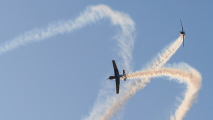 Two aircraft performing aerobatic maneuvers with smoke trails against a clear sky during an aerial aviation display © nilanka