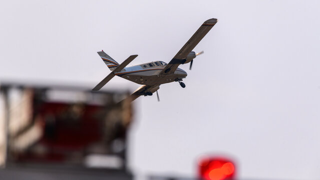 Airplane taking off with landing gear extended against a sky background, with blurred red airport equipment lights in the foreground