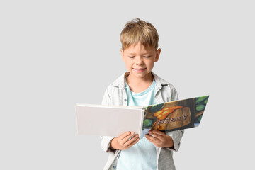 Fototapeta premium Cute little boy reading book on grey background
