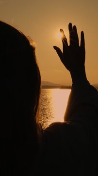 A praying girl stretches out her hand to the sun against the sunset, asking for God's blessing. The concept of aspiration, luck and inspiration. Vertical video.