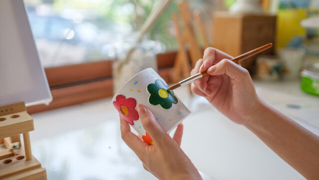 Close up of an artist painting flowers on a handmade mug in a workshop, handmade art and craftsmanship.
