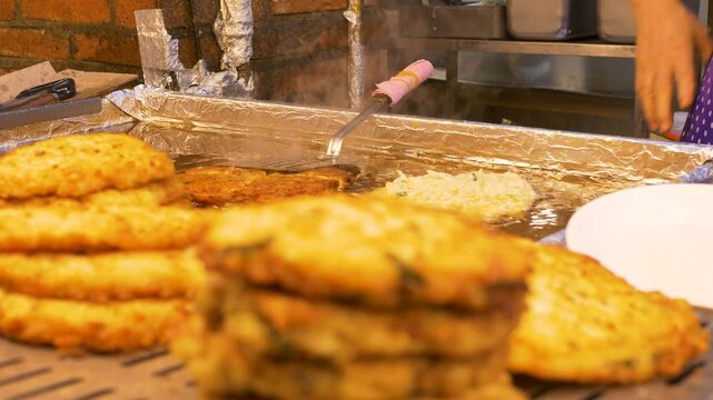 Slow motion close up of woman using cooking utensils forming crispy seafood pancake patty frying in oil on burner stove top at Gwangjang night markets in Seoul city South Korea street food and produce
