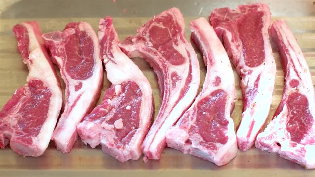 Lamb chops on wooden board being spiced and seasoned before barbecue