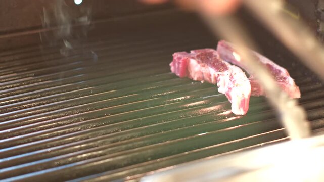 Juicy mutton chops placed on hot grid of outdoor grill with tongs for barbecue