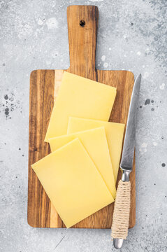 Stack of semi hard yellow cheese slices on rustic wooden cutting board, copy space on gray stone background, dairy ingredient
