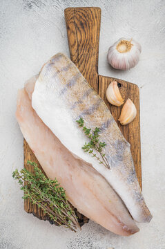Raw pike perch fillets on light background with garlic and thyme, fresh lean freshwater white fish ready for cooking.