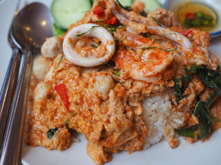Rice topped with seafood curry and creamy egg: steamed rice, squid, shrimp, and fish balls on a plate. It looks delicious. Thai food is very tasty.