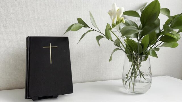 Holy Bible with cross symbol and flowers in glass vase on white background, Christian still life