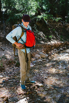 Teen boy hiking with two backpacks on rocks in forest