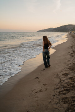 Young woman standing barefoot on beach in wet jeans and black ta