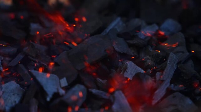 Burning charcoal pieces with bright orange flame, dark blurred background, slow motion