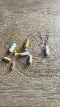 Hand picking up a transparent fish oil capsule from nutrition dietary supplements on a wooden table. Capsules include carnitin, Q10, omega-3 fish oil, vitamin C, vitamin B and ashwagandha.