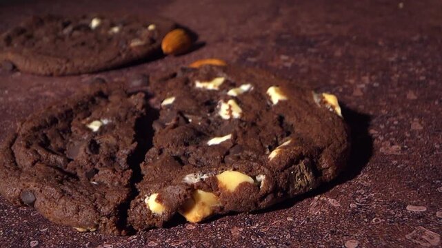 Macro view of a chocolate cookie opening along a crack, revealing soft baked center with chocolate and almond pieces. Detailed texture and crumb captured in close motion.