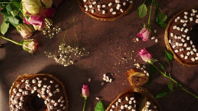 Top view of hands taking a wrapped gift box from a decorated dessert table with donut shaped cakes, flowers and sweets. Festive celebration scene for birthday, Valentine&rsquo;s Day and gift giving.
