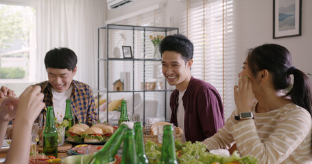 Happy hour good warm summer time diner indoor home. Group of asia people young adult friend man and woman sit at dining table joy fun talk or eat food and drink beer alcohol bottle glass inside house. © ChayTee