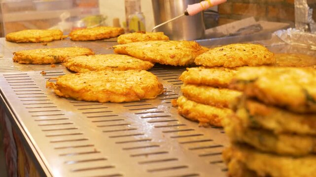 Slow motion close up of battered Bindaetteok seafood pancake patties presented on grill stovetop at night market vendor stall in Gwangjang district Seoul city South Korea Asia street food and cuisine