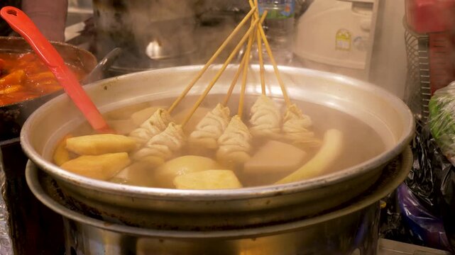 Slow motion close up of Eomukguk Odeng soup broth with skewered fishcakes cooking in large pot filled with hot water at Gwangjang street food night markets in Seoul city South Korea Asian cuisine